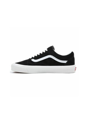 Scarpe da skate in suede nero con accenti e lacci bianchi, caratterizzate da un design low-top e una spessa suola in gomma bianca. Logo Vans visibile sul tallone.