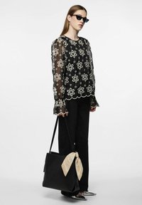 Sort gennemsigtig bluse med hvid blomsterbroderi, lange ærmer med bølgede manchetter, parret med sorte bukser og en sort taske med en beige tørklæde som accent.