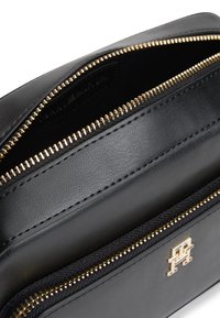 Geantă neagră din piele cu fermoare aurii și un logo metalic auriu pe buzunarul din față, prezentată parțial deschisă.