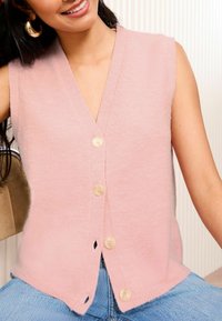 Roze mouwloze cardigan met een diepe V-hals, voorzien van vijf lichte knopen aan de voorkant en een zachte, tekstuurlijke gebreide stof.