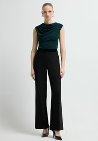 Donkergroen, gedrapeerde top met korte mouwen, gecombineerd met hooggerichte, op maat gemaakte zwarte broek en puntige zwarte hakken. Overal gladde texturen.