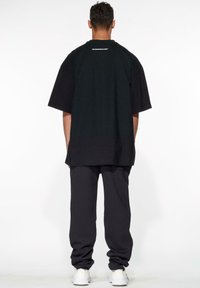 Camiseta negra de gran tamaño con mangas cortas, que presenta un logo blanco en el escote. Combinada con pantalones de chándal oscuros y zapatillas blancas.