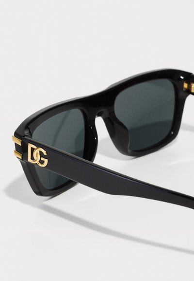 Ochelari de soare cu rame din plastic negru, lentile verzi și accente aurii pe tâmple, având logo-ul "DG". Design unghiular și îndrăzneț.