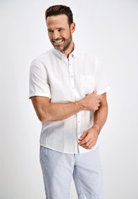 Camisa blanca de manga corta con cuello abotonado y bolsillo en el pecho, combinada con pantalones cortos a rayas azul claro. Textura suave, diseño casual.