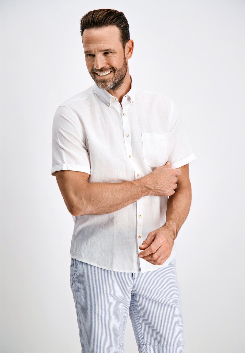 Camisa blanca de manga corta con cuello abotonado y bolsillo en el pecho, combinada con pantalones cortos a rayas azul claro. Textura suave, diseño casual.