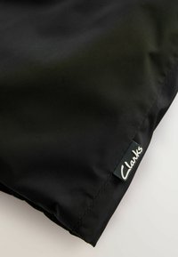 Sort stofpose med en glat tekstur, der har en syet kant og en lille sort etiket med hvid tekst, "Clarks," hæftet på.