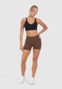 Zwarte sportbh met verstelbare banden en een geplooide voorkant, gecombineerd met hoge, bruin korte broek. Beide gemaakt van rekbare stof.