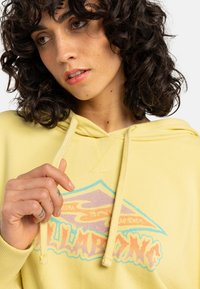 Yellow hoodie with a blue and pink graphic design featuring waves. Soft texture, adjustable drawstring, and ribbed cuffs.