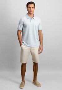 Lyseblå polo med korte ermer, parret med beige shorts og lysebrune slip-on sko. Enkelt design og avslappet passform.