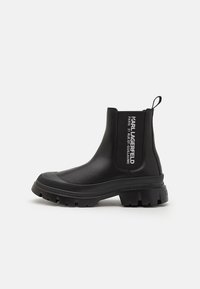 Botines negros de tobillo hechos de goma suave con una suela gruesa, paneles laterales elásticos y detalles del logo en blanco en el tubo.