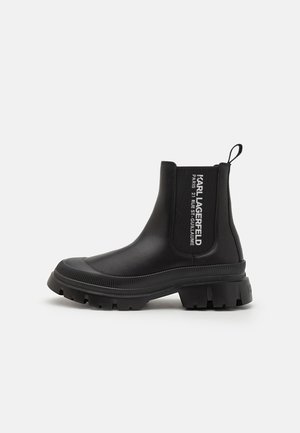 Black ankle boots made of smooth rubber with a chunky sole, elastic side panels, and logo detailing in white on the shaft.