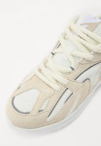 Sneaker met een combinatie van lichtbeige suede en mesh bovenwerk, witte rubberen zool en gestructureerde veters. Heeft een gestroomlijnd ontwerp.