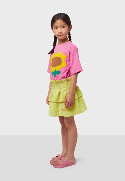 Pink cotton t-shirt with a sunflower graphic, paired with a frilled lime green skirt featuring a checkered pattern. Pink sandals with a pattern.