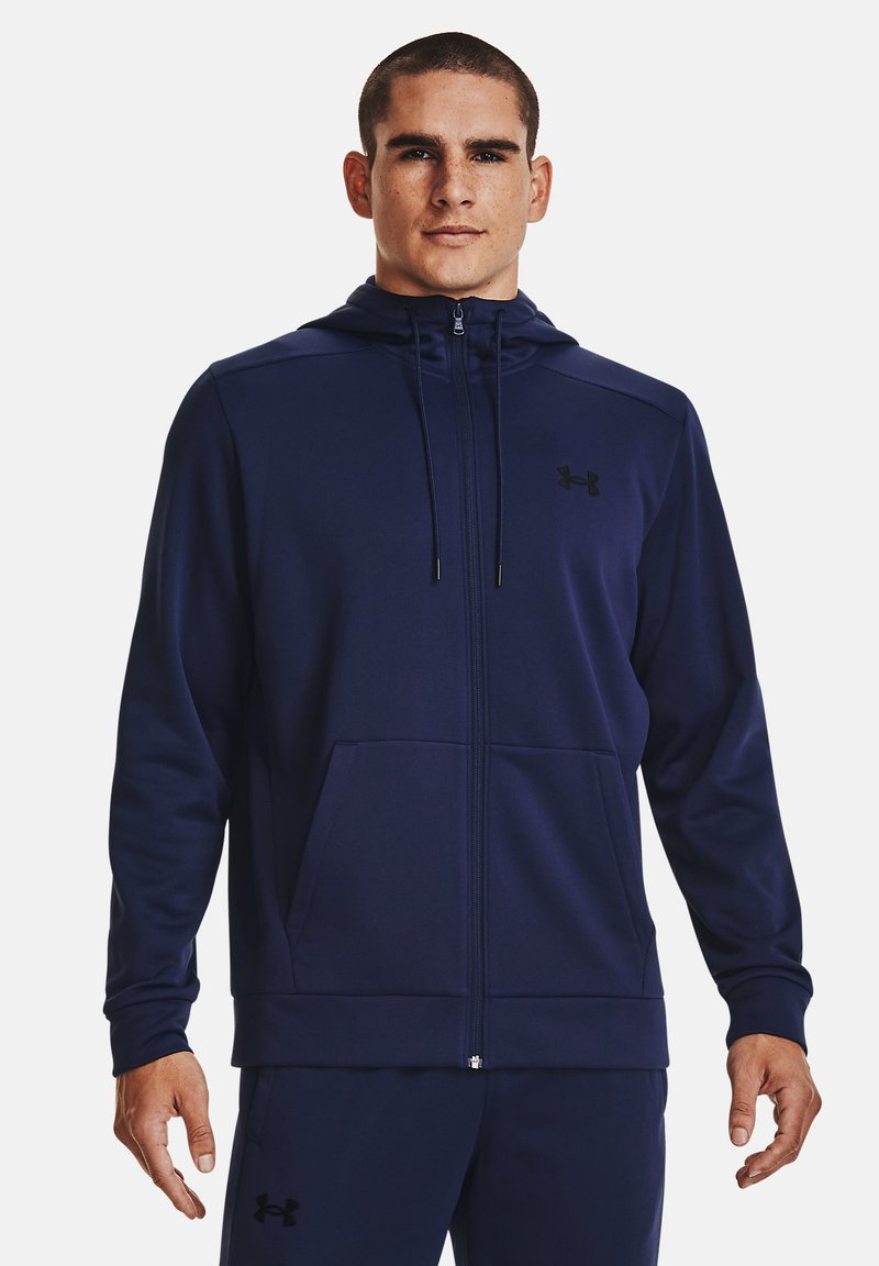Námořnická modrá mikina na zip z měkkého materiálu, s přední kapsou, nastavovací kapucí a černým logem na hrudi. Hladký povrch.