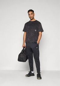 Must triiksärk, lahtise lõikega, väikese logoga; mustad Nike jooksupüksid kitsenevate säärtega; mustad tossud ja must spordikott.