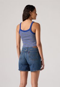 Juostuotas mėlynas tank topas su plačiomis petnešėlėmis, derinamas su aukštu liemeniu tamsiai mėlynomis džinsinėmis šortais, turinčiais užpakalinius kišenes ir firminį odinį ženklelį.