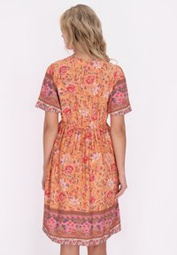 Oranje bloemenjurk met korte mouwen, een taille die is gecinched en een patroon aan de onderrand. Heeft roze en paarse accenten door het stofontwerp.