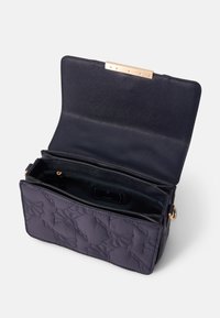Borsa a spalla trapuntata blu navy con finitura testurizzata, chiusura in hardware dorato e interno aperto. L'interno presenta un'etichetta e una tasca con zip.