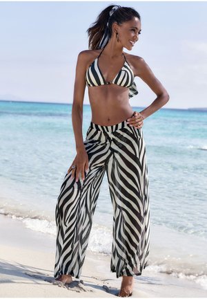 Bikini a strisce bianche e nere con top triangolare, abbinato a pantaloni fluide e trasparenti con un motivo a strisce zebra simile.