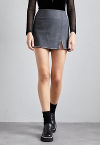 Minifalda de lana gris con una abertura en el frontal y adornada con tachuelas plateadas a lo largo del dobladillo, combinada con calcetas negras y zapatos gruesos.