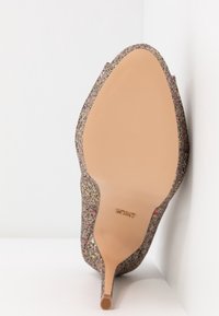 Escarpin à bout pointu recouvert de paillettes multicolores avec une semelle beige lisse, photographié en contre-plongée sur fond blanc.