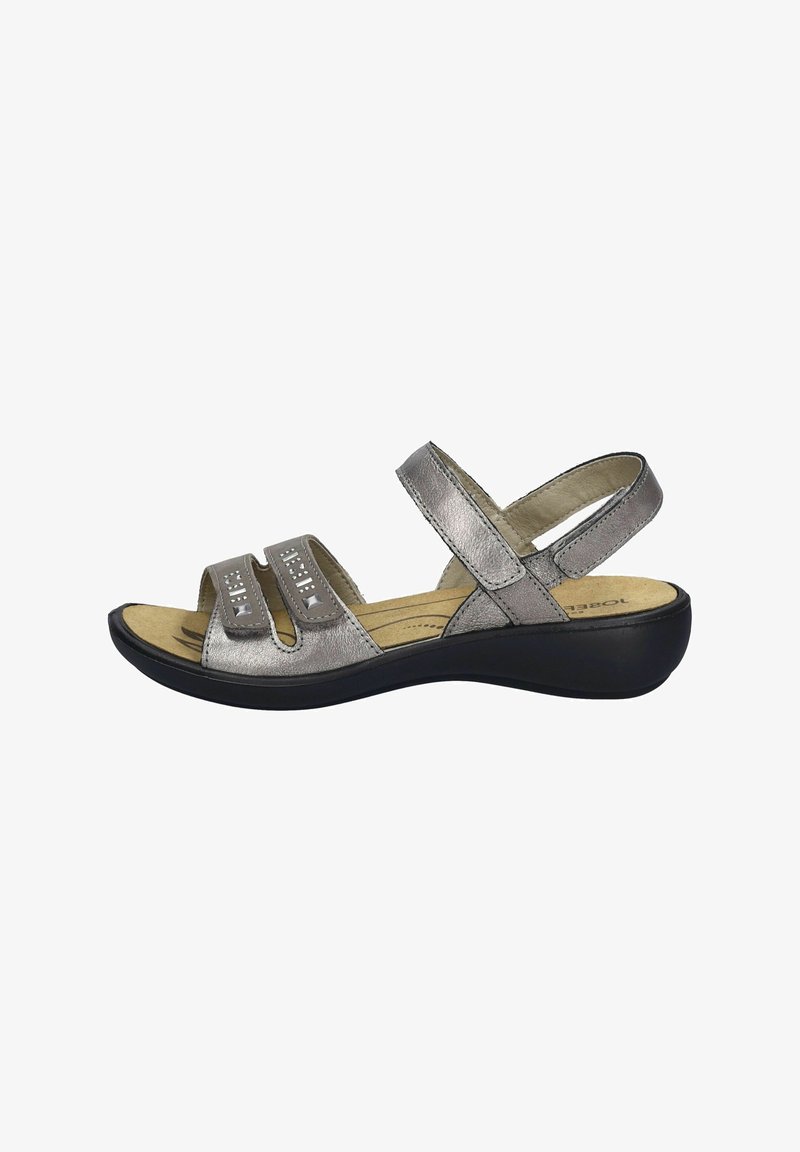 Srebrne metaliczne sandały z dwoma szerokimi paskami z przodu, regulowanym paskiem na plecach, wyściółką z miękkiego materiału oraz czarną gumową podeszwą.