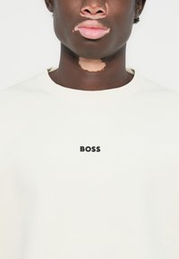 Sudadera color crema con cuello redondo y logo negro "BOSS" en el pecho. Confeccionada en material suave y con una textura lisa.