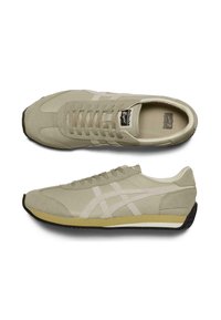 Ljusgrå sneakers med en texturerad ovandel, vita detaljer och en mörk gummisula. Inkluderar snörningssystem och varumärke på tungan.