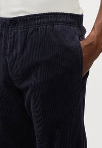 Pantalons en velours côtelé marine avec des côtes verticales, dotés d'une taille élastique et de poches latérales. La texture du tissu est douce et doublée.
