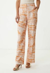 Pantalon large en mélange de lin avec un motif abstrait orange et blanc, doté de poches avant et d'une taille ajustée. Sandales à talons argentés visibles.