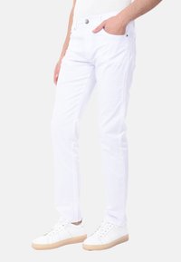 Jeans bianchi in cotone con vestibilità slim, dotati di cinque tasche, chiusura con bottone e una texture liscia. Abbinati a sneakers bianche e un top leggero.