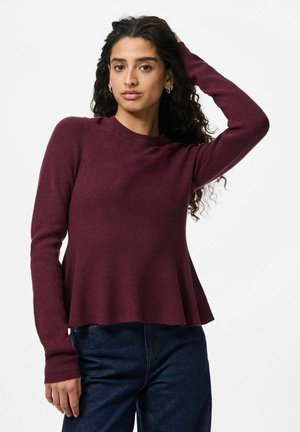 Pull en tricot côtelé bourgogne à manches longues et à ourlet évasé, associé à un pantalon en denim foncé. Texture douce et design simple.
