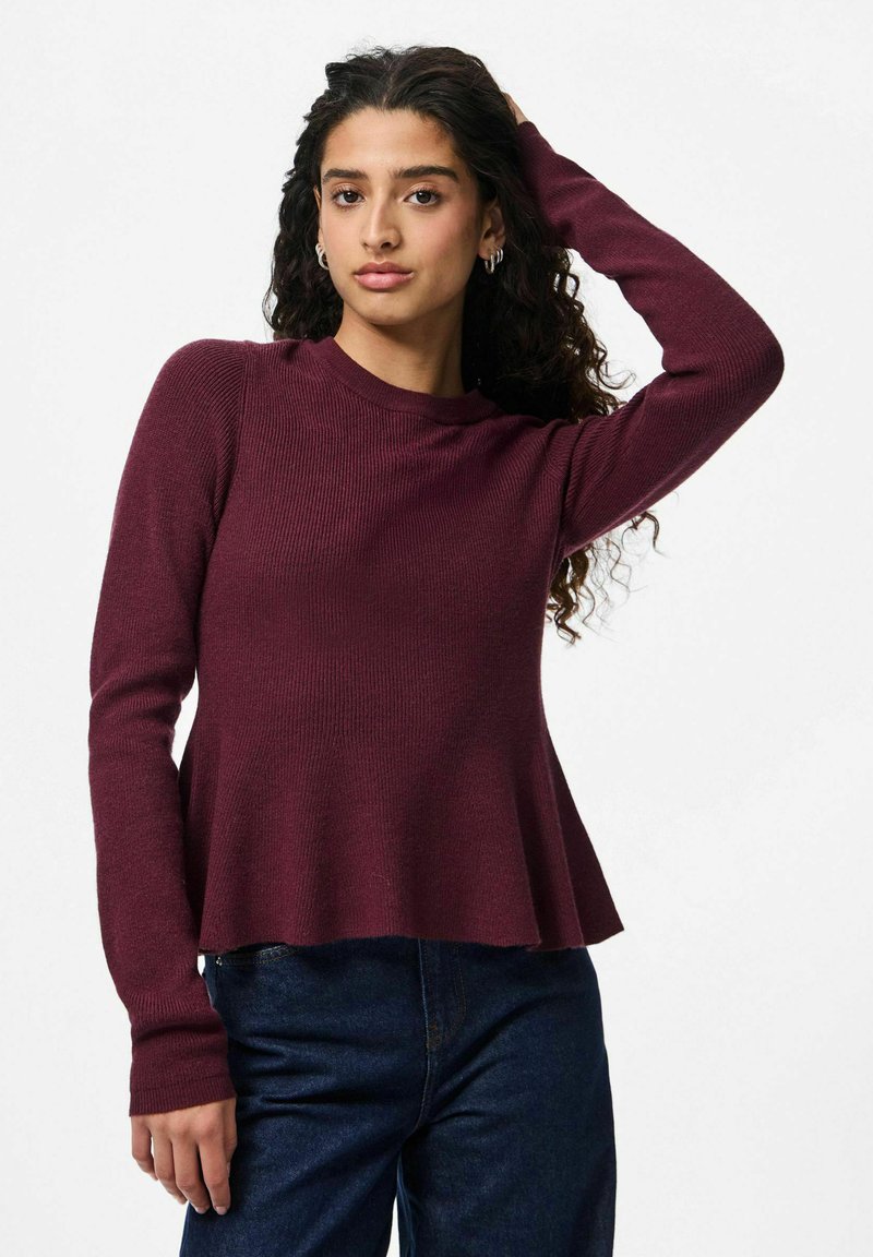 Burgundijas krāsas ribota adīta džemperis ar garām piedurknēm un paplašinātu apakšdaļu, apvienots ar tumšām džinsu biksēm. Mīksta tekstūra un vienkāršs dizains.