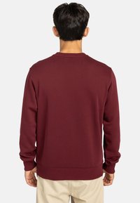Bordeaux sweatshirt, crewneck design, ribbede manchetter og kant, glat tekstur, ensfarvet, ingen synlige logoer eller mønstre.