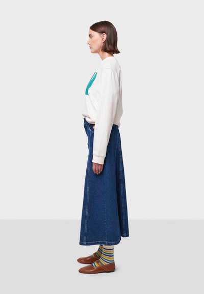Felpa bianca con grafica turchese, gonna di jeans a vita alta, calzini a righe multicolori e scarpe slip-on marroni. Vista laterale.