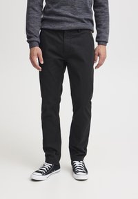 Sorte bomullsbukser med rett benpassform, med frontlommer og et minimalt design. Kombinert med sorte kanvas sneakers.