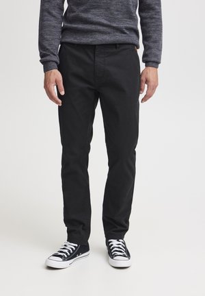 Schwarze Baumwollhosen mit einem geraden Schnitt, ausgestattet mit frontalen Taschen und einem minimalistischen Design. Kombiniert mit schwarzen Canvas-Sneakern.