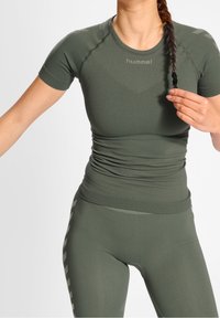 Kortärmad, figurnära atletisk topp i olivgrön, tillverkad av strukturväv med sömlös design och logotyp på bröstet.