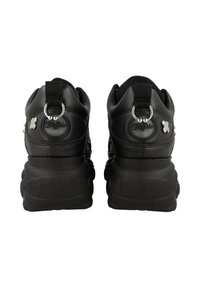 Zapatillas negras con una suela gruesa, con un upper de cuero suave, acentos moldeados y una lengüeta en el talón. Detalles en hardware plateado presentes.