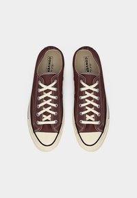 Ζευγάρι μπορντό χαμηλά πάνινα παπούτσια με λευκές λαστιχένιες μύτες και κρεμμύδι κορδόνια, από πάνω σε λευκό φόντο.