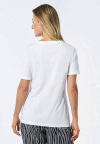 Weiße Kurzarm-T-Shirt mit Rundhalsausschnitt, glatter Textur und hochgekrempelten Ärmeln. Tragen zu gemusterten schwarz-weißen Hosen.