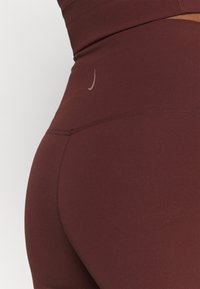 Bordowe legginsy wykonane z gładkiego, elastycznego materiału. Posiadają małe, tonalne logo oraz podwójne szwy na pasie i szwach nogawek.