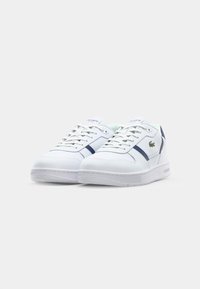 Zapatillas blancas con parte superior de cuero suave, acentos azules en el lateral y suela de goma texturizada. Presenta el logo de la marca en la lengüeta.