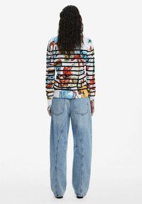 Bunt gemusterte Langarmbluse mit floralen Motiven und horizontalen Streifen, kombiniert mit locker sitzenden hellblauen Denim-Jeans und sichtbaren Nähdetails.