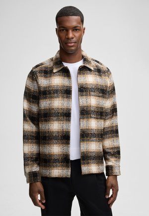 Plaid jacket in brown, black, and cream colors, featuring a button-front, collared design, and textured fabric. White t-shirt underneath.