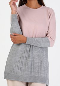 Maglione a maniche lunghe con texture a coste; la parte superiore rosa si trasforma in una parte inferiore grigia con costine verticali e un collo rotondo.