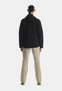 Czarna wodoodporna kurtka z kapturem, o luźnym kroju i teksturowanej, gładkiej powierzchni; w zestawie z jasnobeżowymi spodniami cargo.