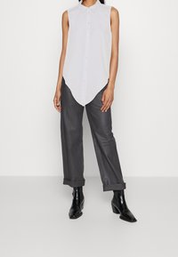 Camicia bianca senza maniche con colletto a punta, caratterizzata da un orlo curvo. Abbinata a pantaloni grigio ardesia arrotolati e stivali neri con tacco.