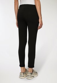 Czarne, dopasowane legginsy o gładkiej teksturze i elastycznym pasku w talii, połączone z jasnymi, sportowymi trampkami z szarymi akcentami.