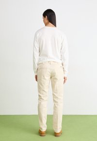 Pantaloni de culoare crem, design cu picioare drepte, din material de bumbac. Au buzunare la spate și un ușor luciu, asortați cu un top alb cu mâneci lungi.